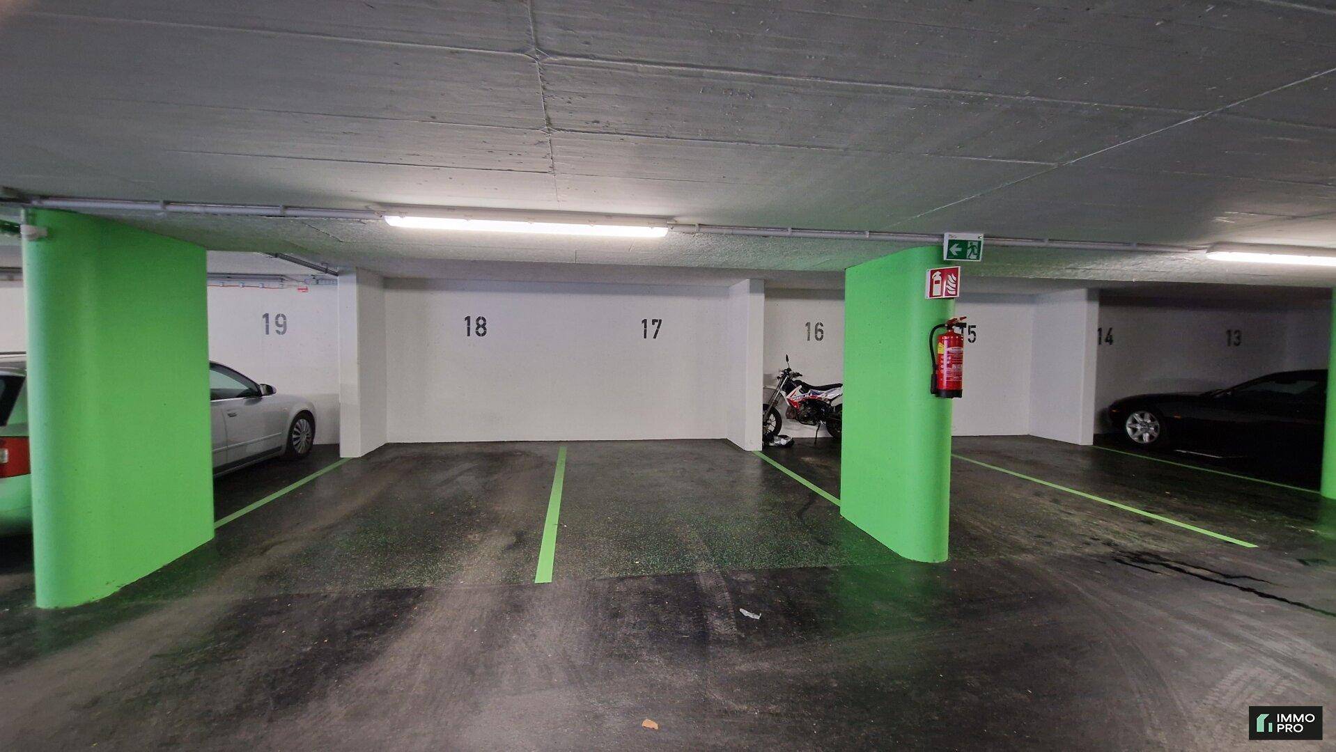 Tiefgarage mit nummerierten Stellplätzen, grünen Säulen und geparkten Fahrzeugen.