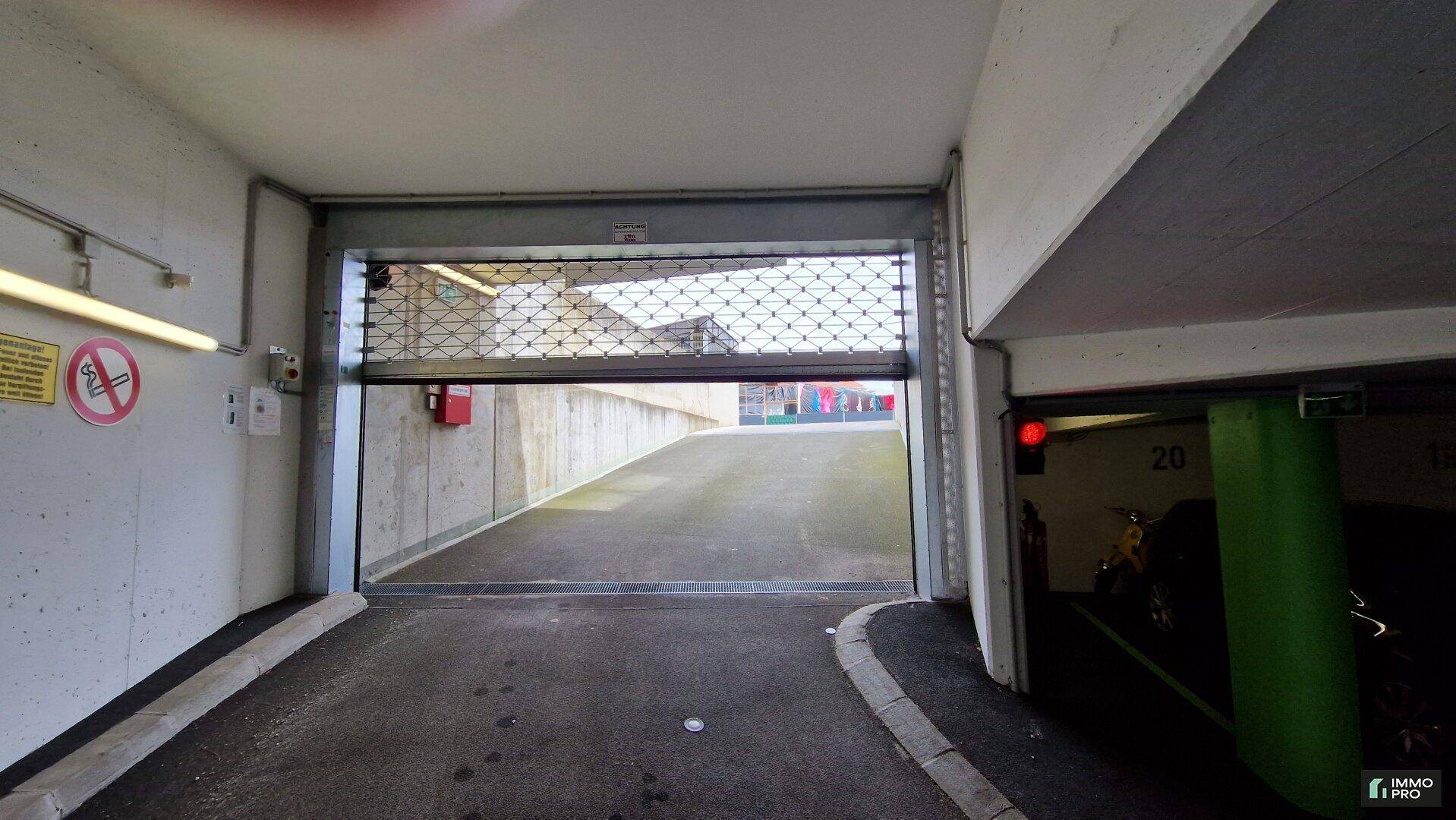 Blick aus der Tiefgarage auf die Ausfahrt mit einem Metallrolltor und Rampe.