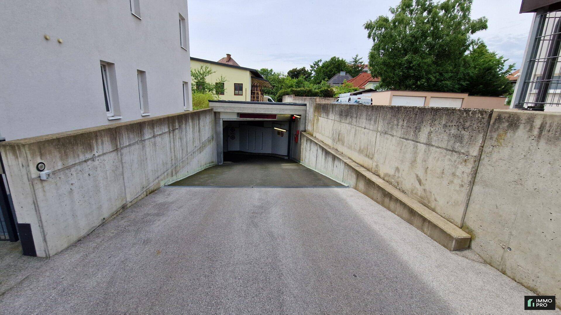 Einfahrt zu einer Tiefgarage mit Betonwänden und einer leicht abfallenden Rampe.