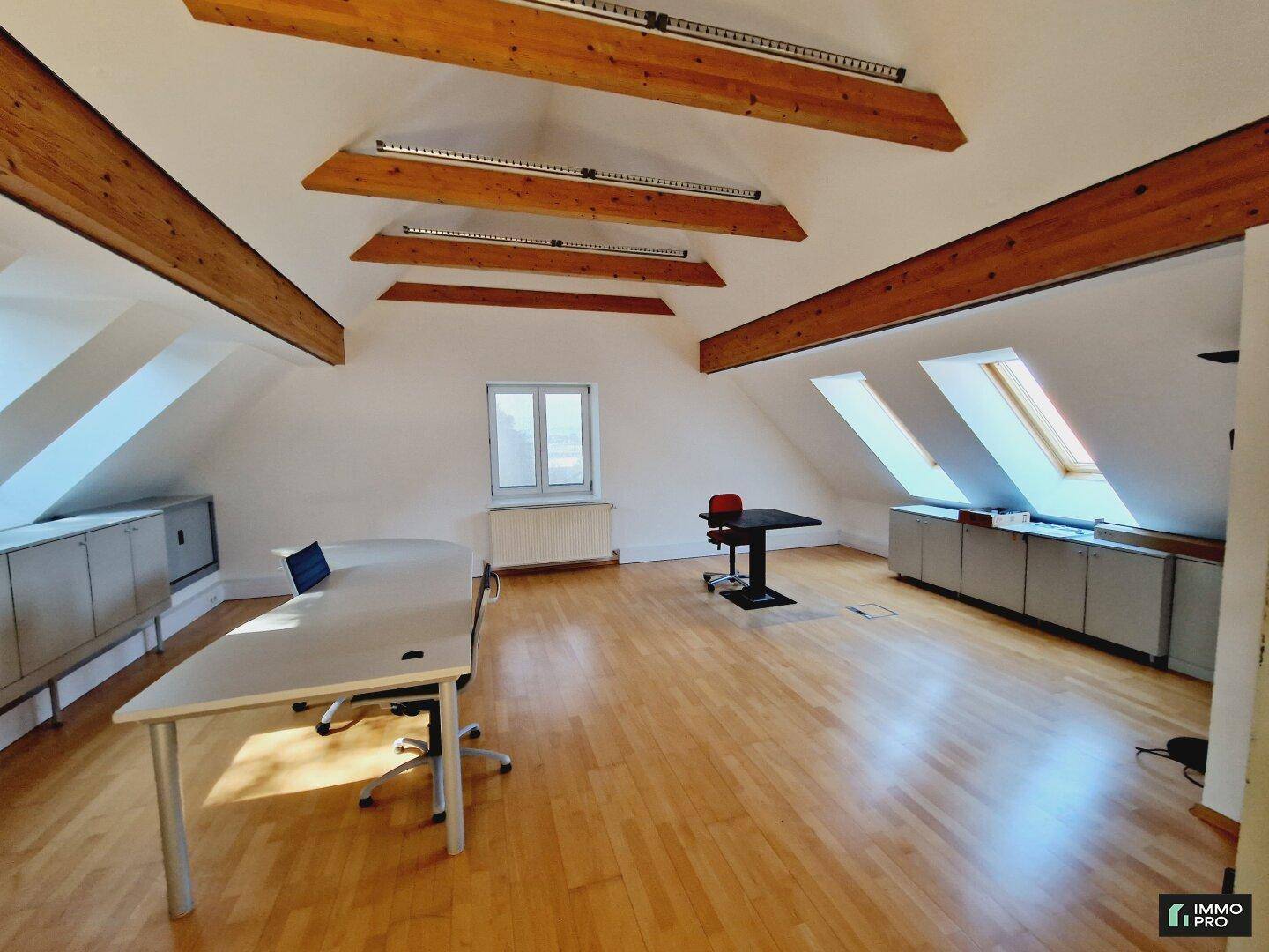 Geräumiger Büroraum im Dachgeschoss mit Holzboden, Schränken und mehreren Fenstern für viel Licht.
