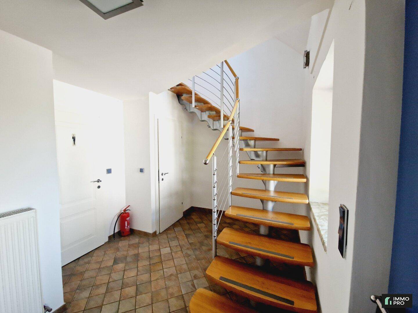Elegante Holztreppe mit Metallgeländer führt in den oberen Bereich, umgeben von Terrakottafliesen.