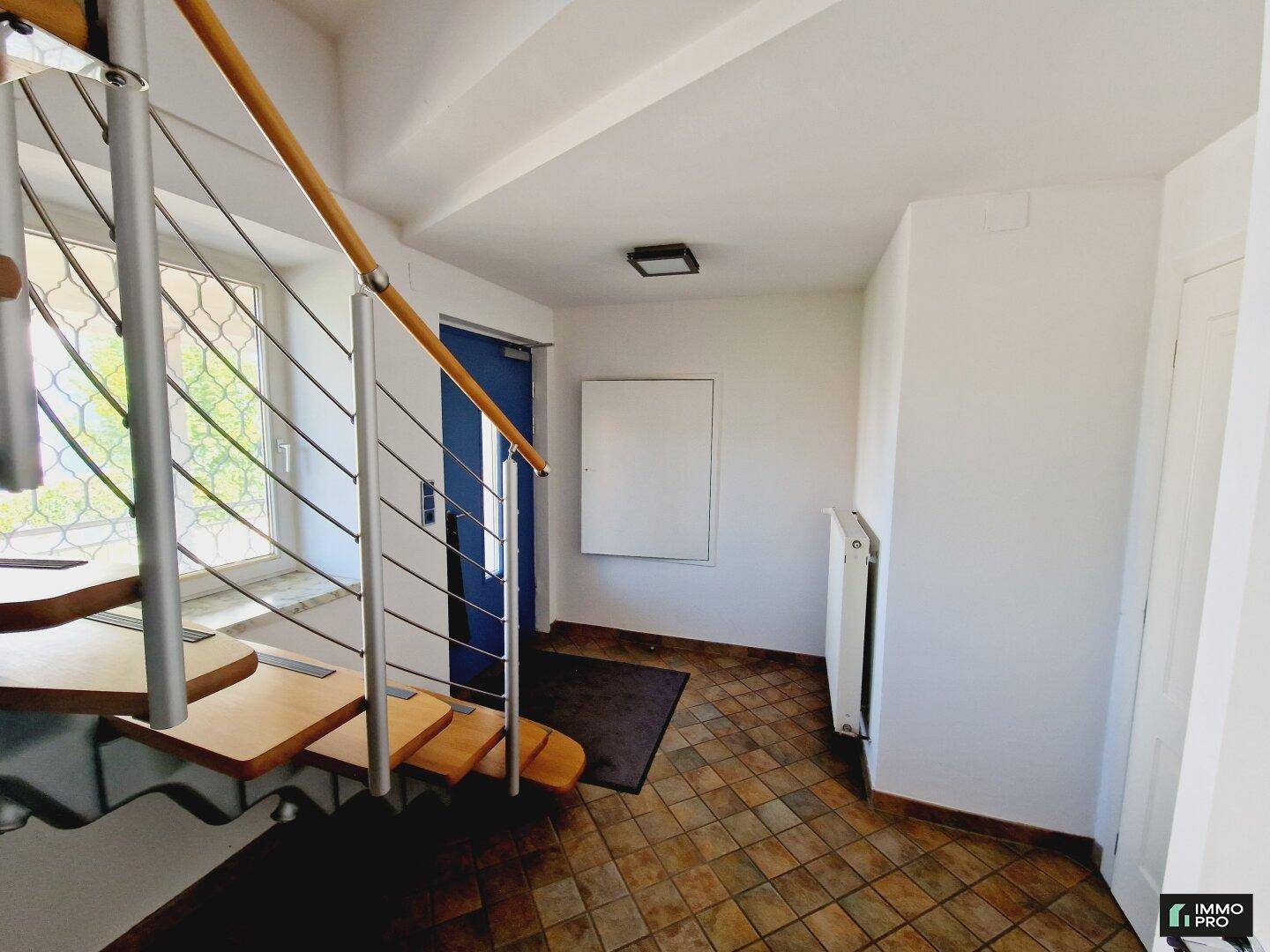 Eingangsbereich mit Terrakottafliesen und einer modernen Holztreppe, die zu den oberen Etagen führt.