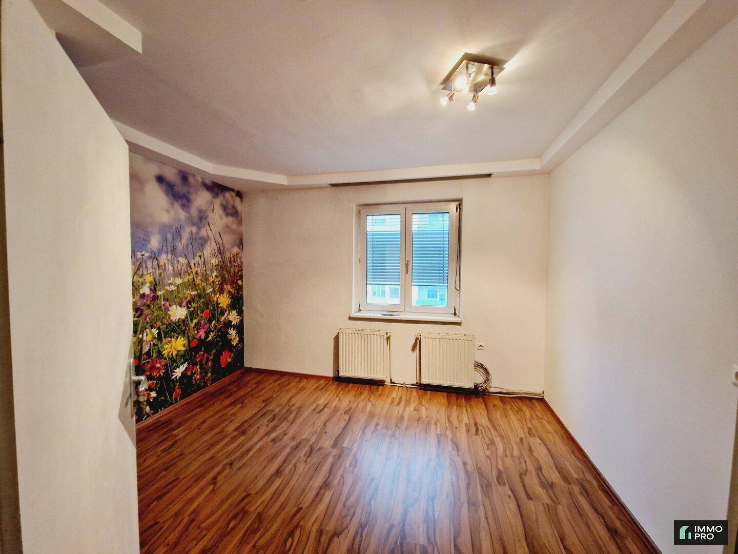 Helles Schlafzimmer mit Laminatboden, Fenster und einer dekorativen Blumenwandtapete.