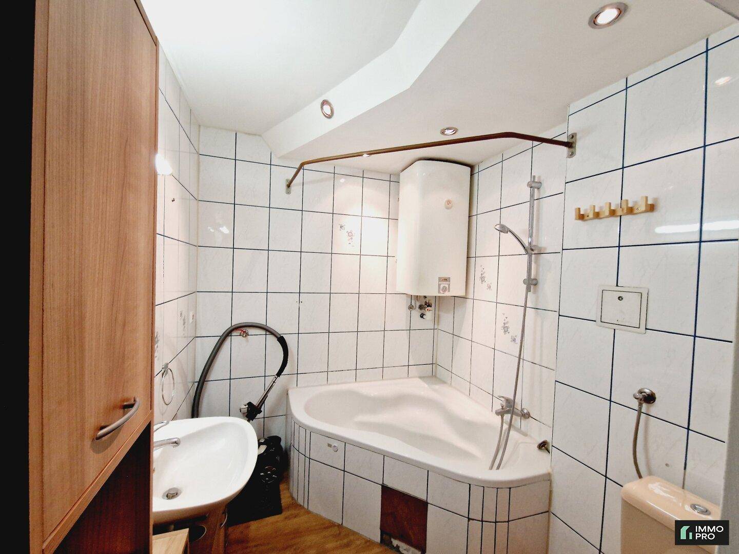 Badezimmer mit weißen Fliesen, einer Eckbadewanne, Waschbecken und Toilette.