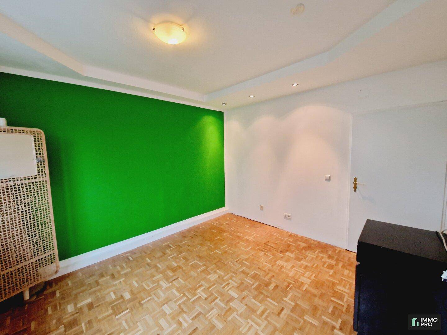 Geräumiges Zimmer mit Parkettboden und leuchtend grüner Wand, bietet vielseitige Nutzungsmöglichkeiten.