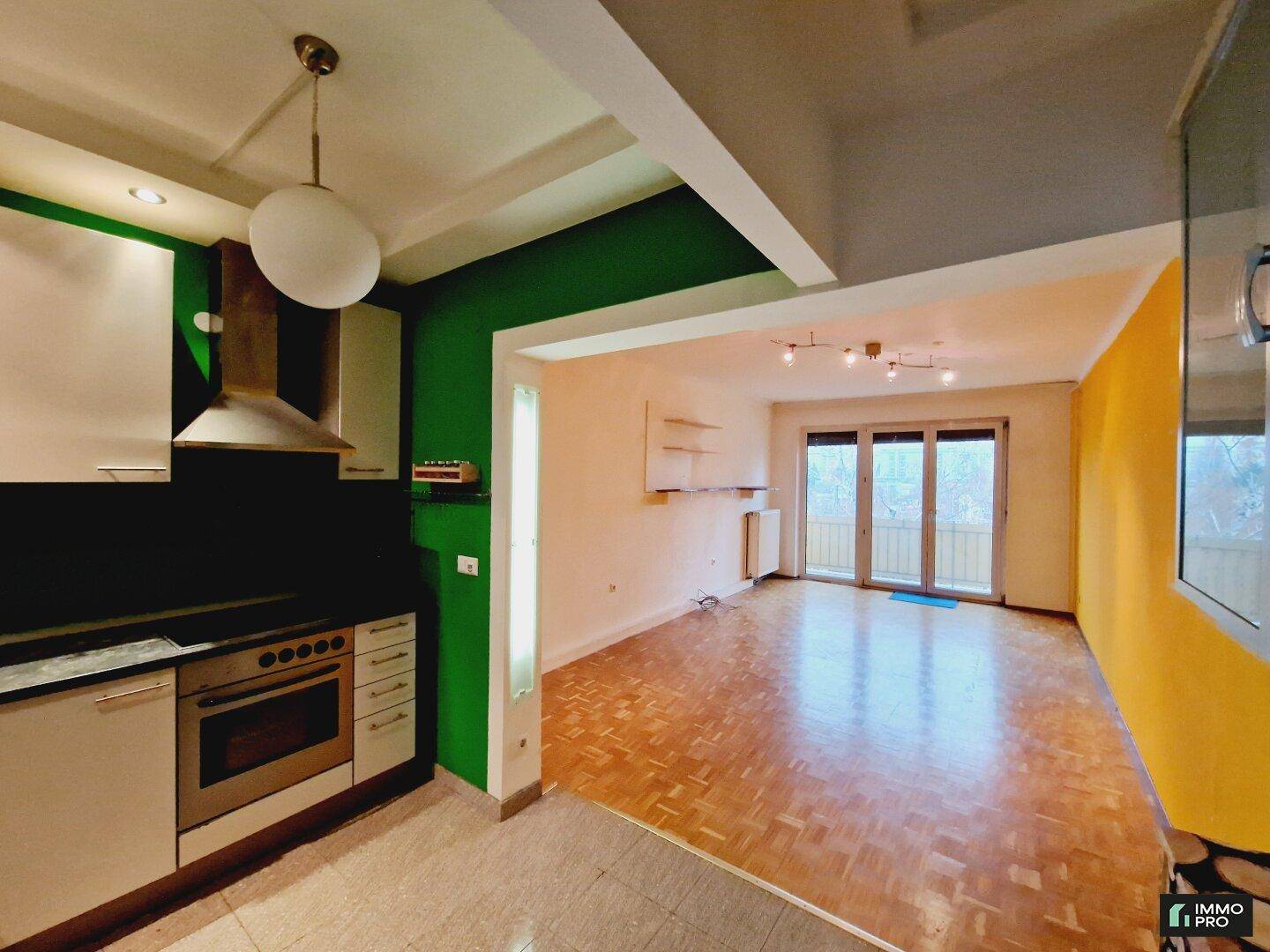Offener Wohn-Essbereich mit integrierter Küche, Parkettboden und Zugang zum Balkon.