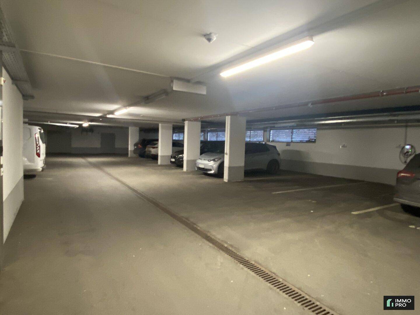 Geräumige Tiefgarage mit mehreren Stellplätzen, Betonboden und Deckenbeleuchtung.