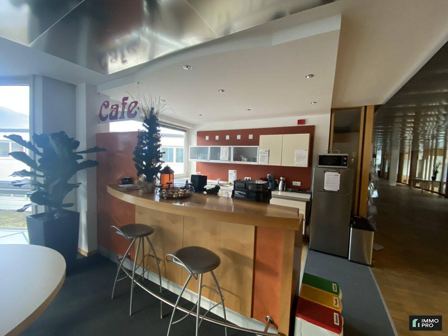 Kleine Café-Ecke mit Theke, Barhockern, Kühlschrank und Mikrowelle in einem hellen Raum.
