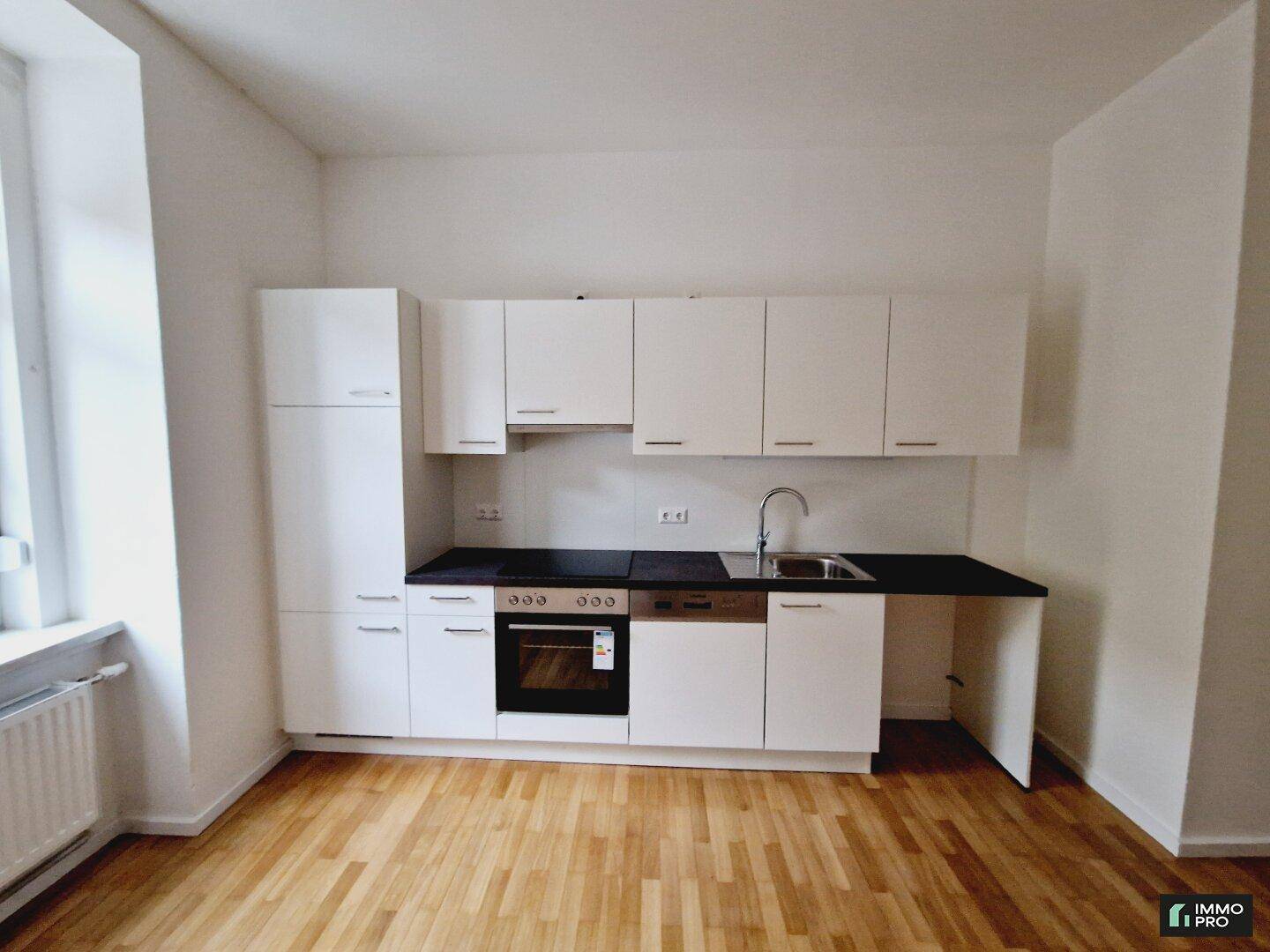 Moderne Küchenzeile mit weißen Schränken, schwarzer Arbeitsplatte, Spüle und integriertem Backofen, sehr funktional.