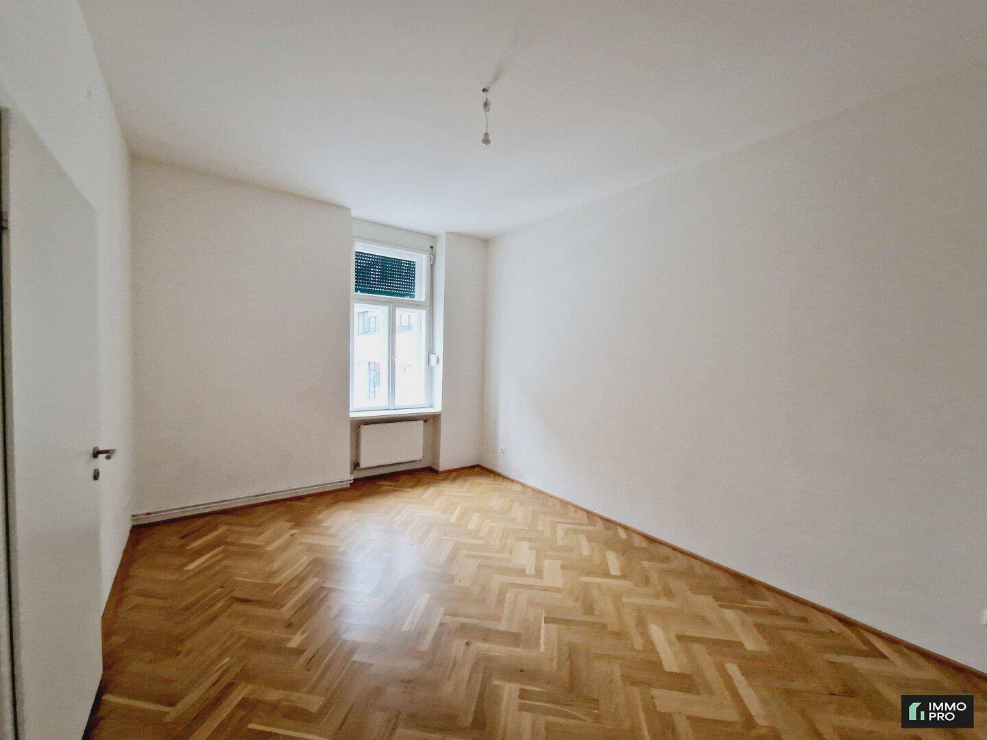 Ruhiges Schlafzimmer mit klassischem Fischgrätparkett, weißen Wänden und einem Fenster für natürliche Belichtung.