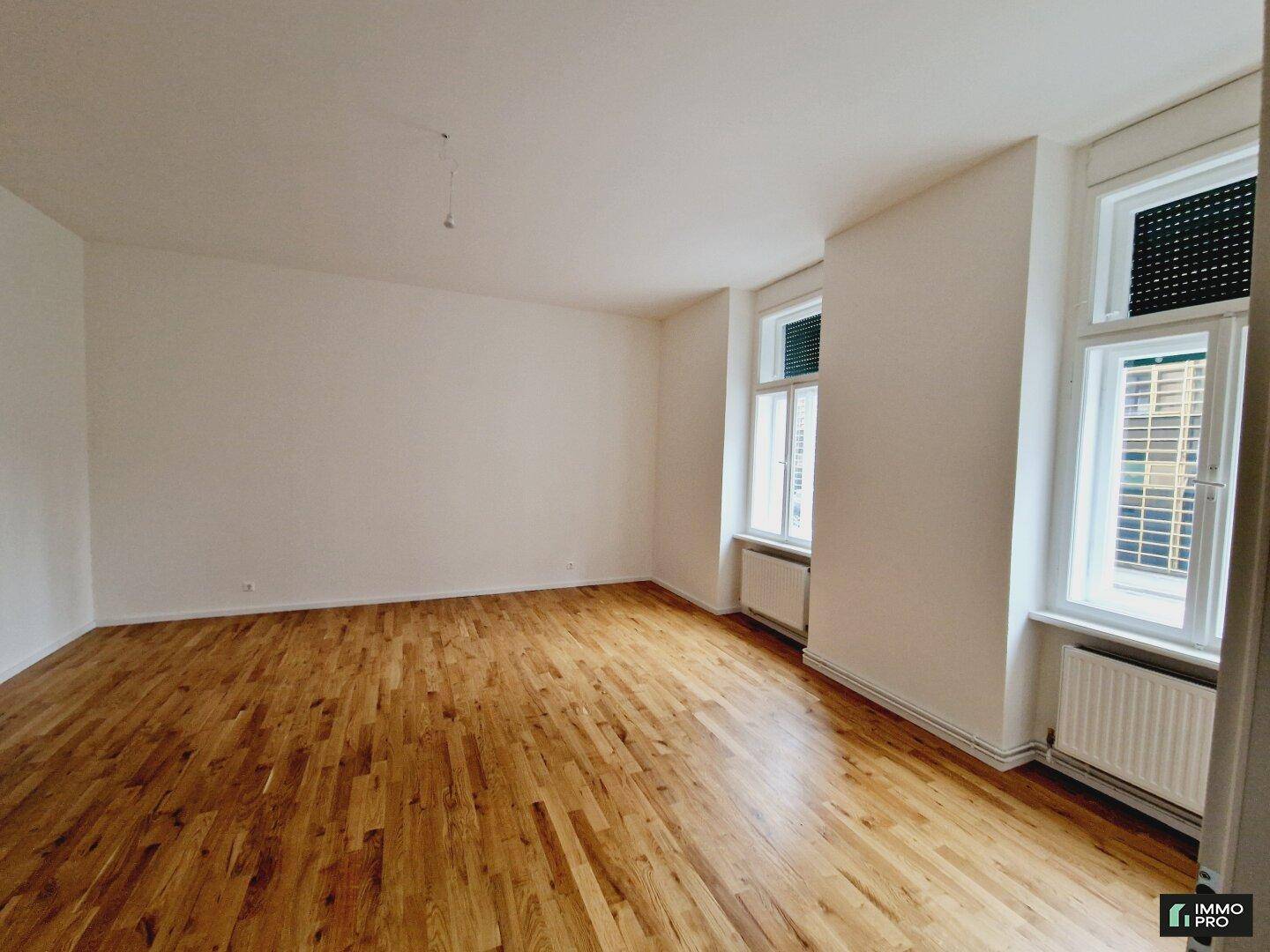Helles Zimmer mit Holzboden, weißen Wänden und zwei Fenstern, bereit zur individuellen Gestaltung und Einrichtung.