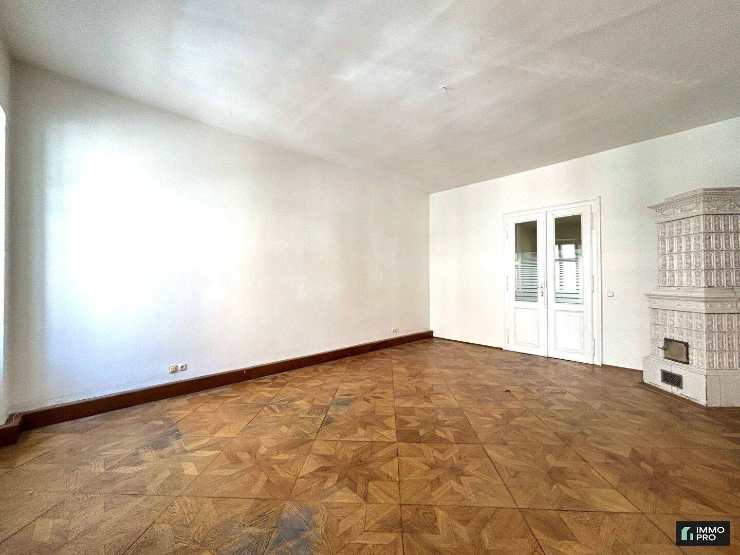Heller Wohnraum mit klassischem Parkettboden und einem dekorativen Kachelofen, bereit zur individuellen Gestaltung.