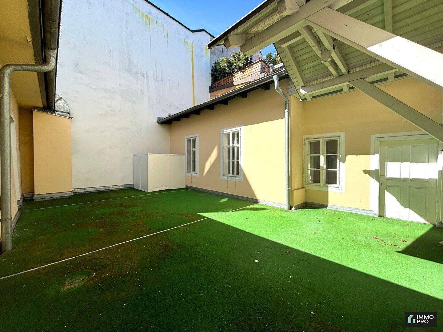 Sonniger Innenhof mit Kunstrasen und gelb gestrichenen Fassaden, bietet einen privaten Außenbereich.