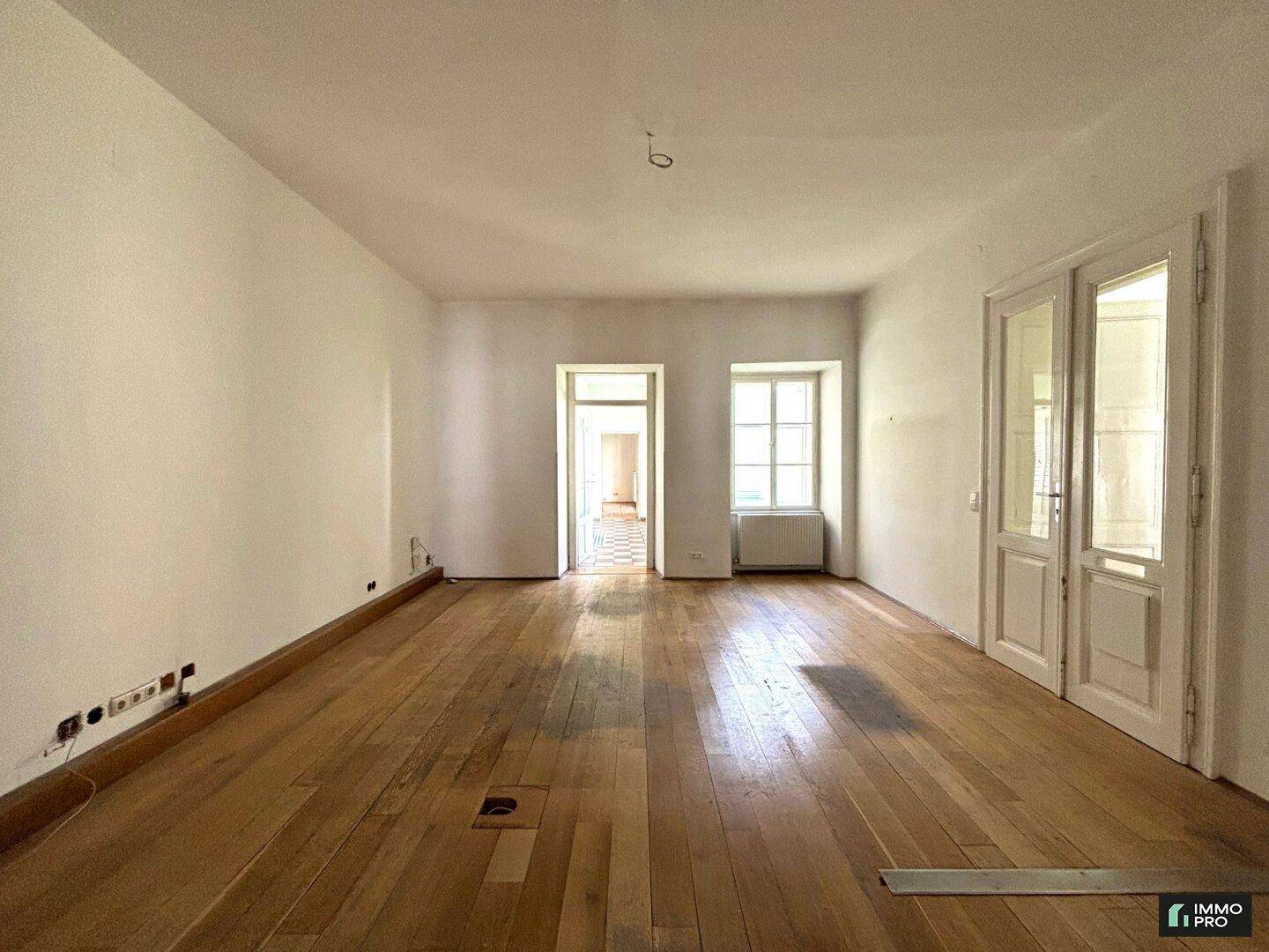 Geräumiger Wohnbereich mit Holzboden und doppelten Flügeltüren, die zu einem weiteren Raum führen.