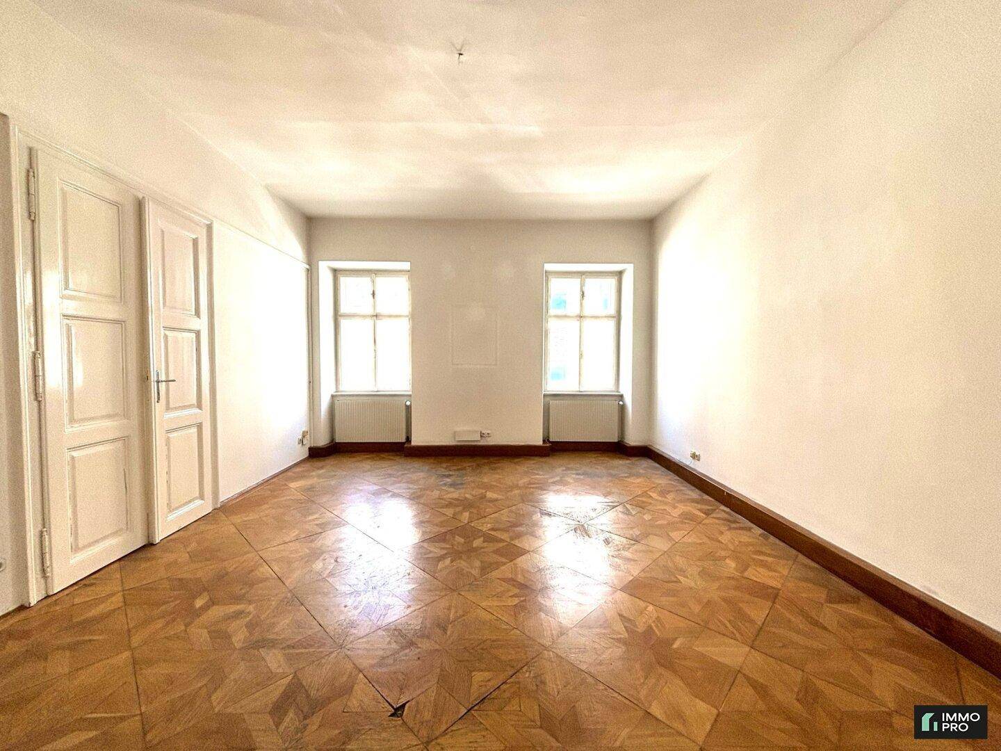 Helles Zimmer mit klassischem Parkettboden und zwei Fenstern, ideal für ein Schlaf- oder Arbeitszimmer.