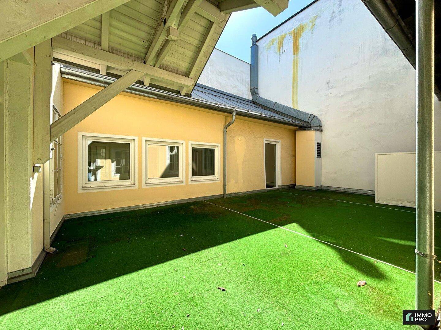 Weitläufige Terrasse mit Kunstrasen und Blick auf die umliegenden Gebäude, teilweise überdacht.