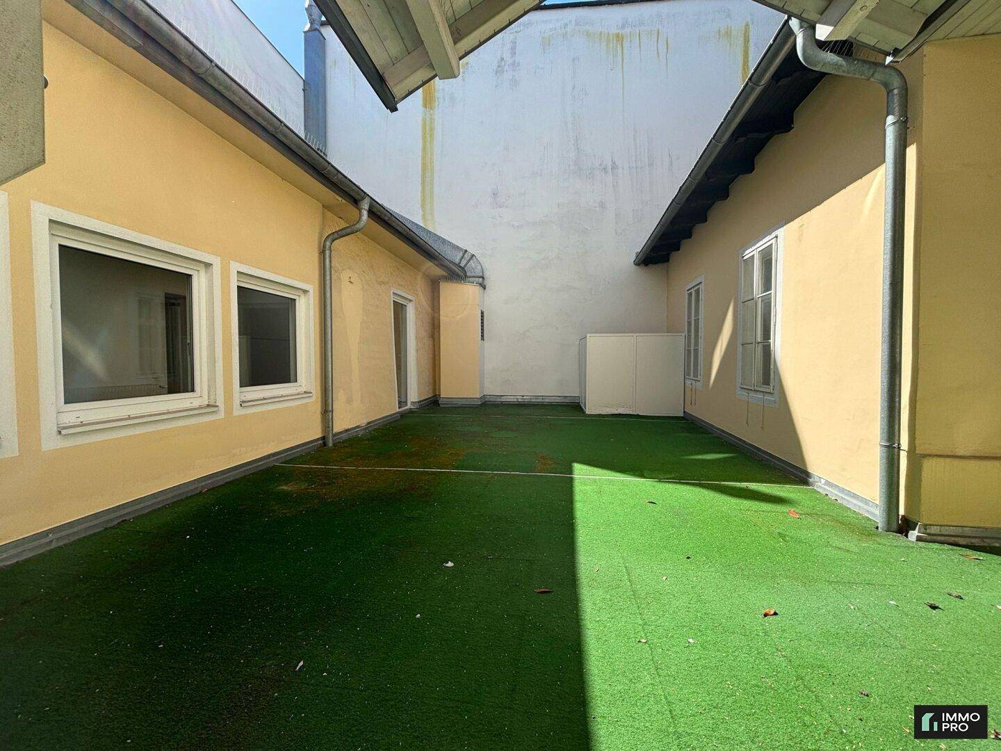 Großer Innenhof mit Kunstrasenfläche, umgeben von Gebäuden, ideal für Entspannung im Freien.