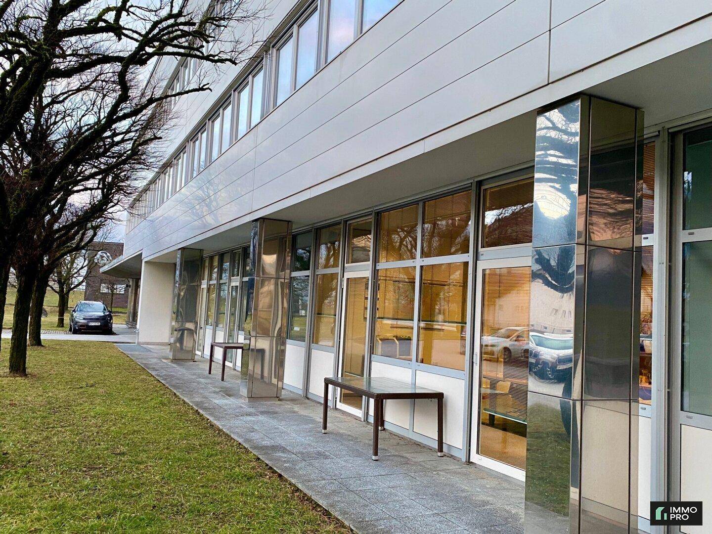 Erdgeschossfassade des Gebäudes mit großen Schaufenstern und einem gepflasterten Gehweg.
