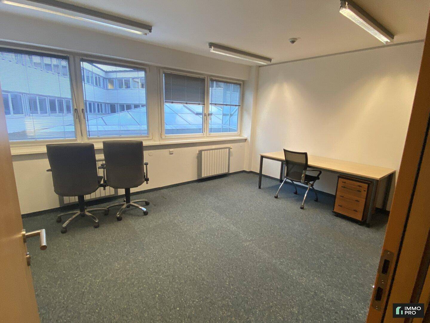 Leeres Büro mit Schreibtisch, Bürostühlen und Fenstern mit Jalousien, bereit zur Nutzung.