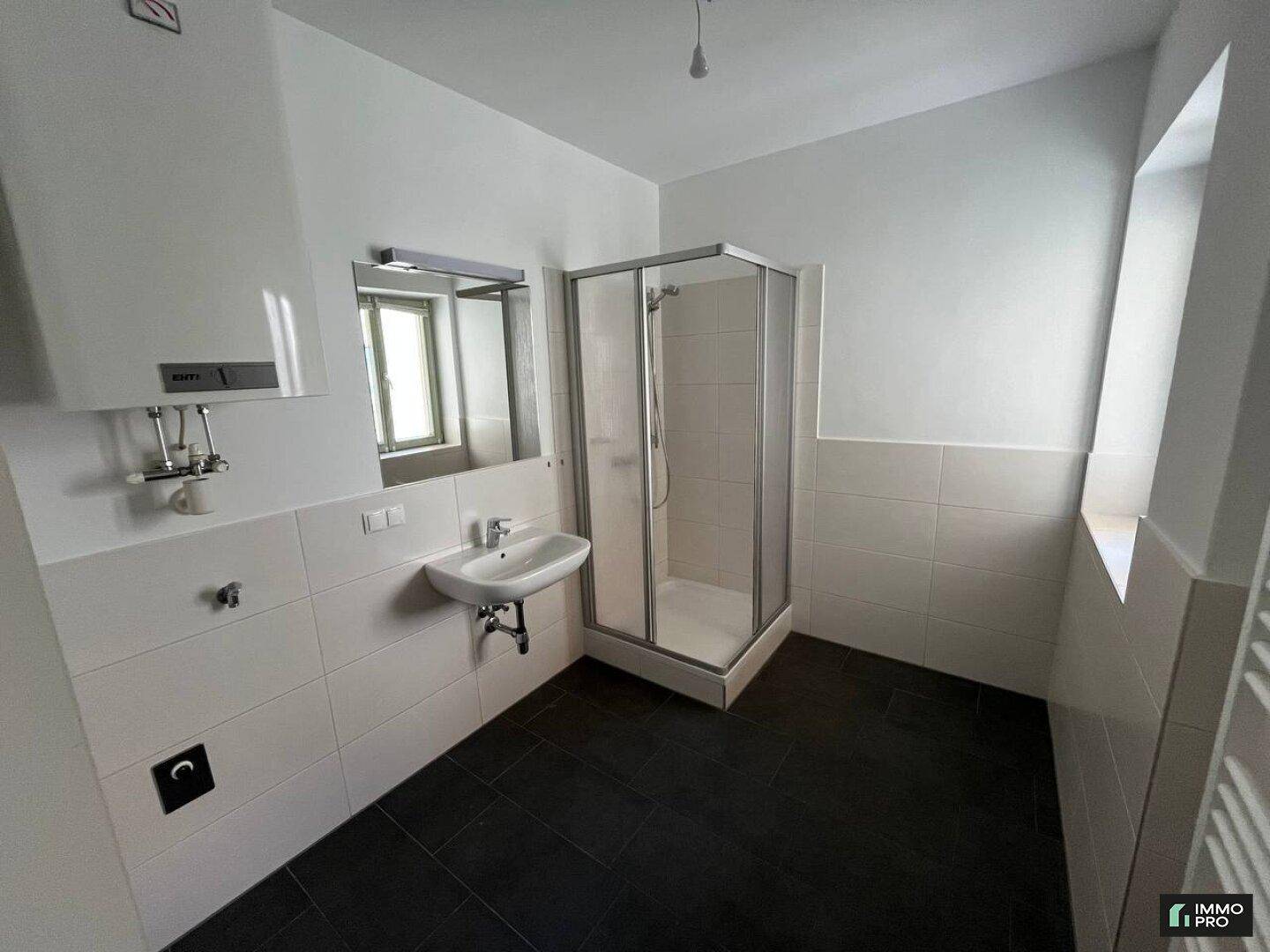 Modernes Badezimmer mit dunklen Fliesen, Duschkabine, Waschbecken und einem Fenster für Belüftung.