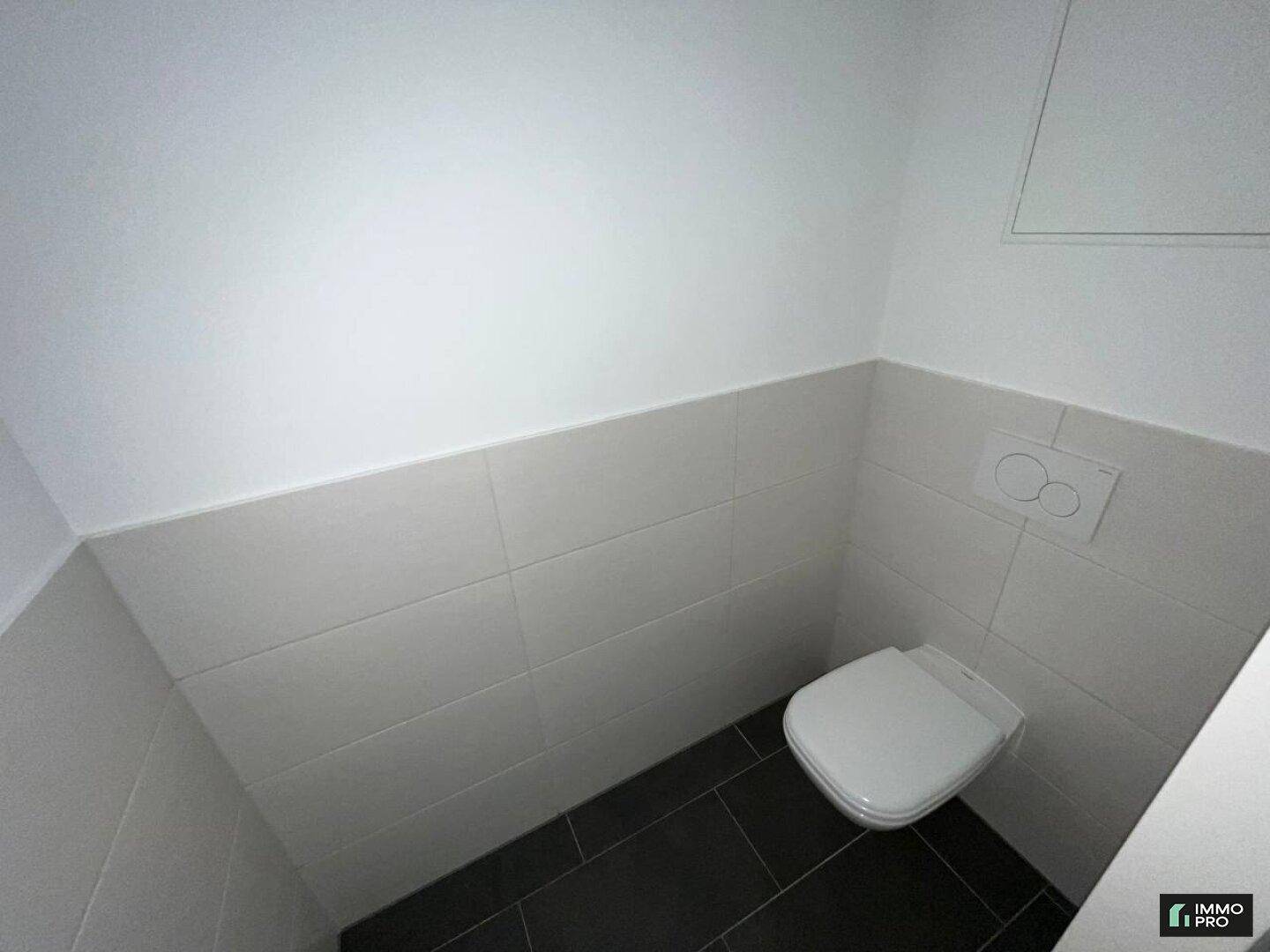 Kleines Gäste-WC mit dunklen Fliesen, halbhohen weißen Wandfliesen und wandhängendem WC.