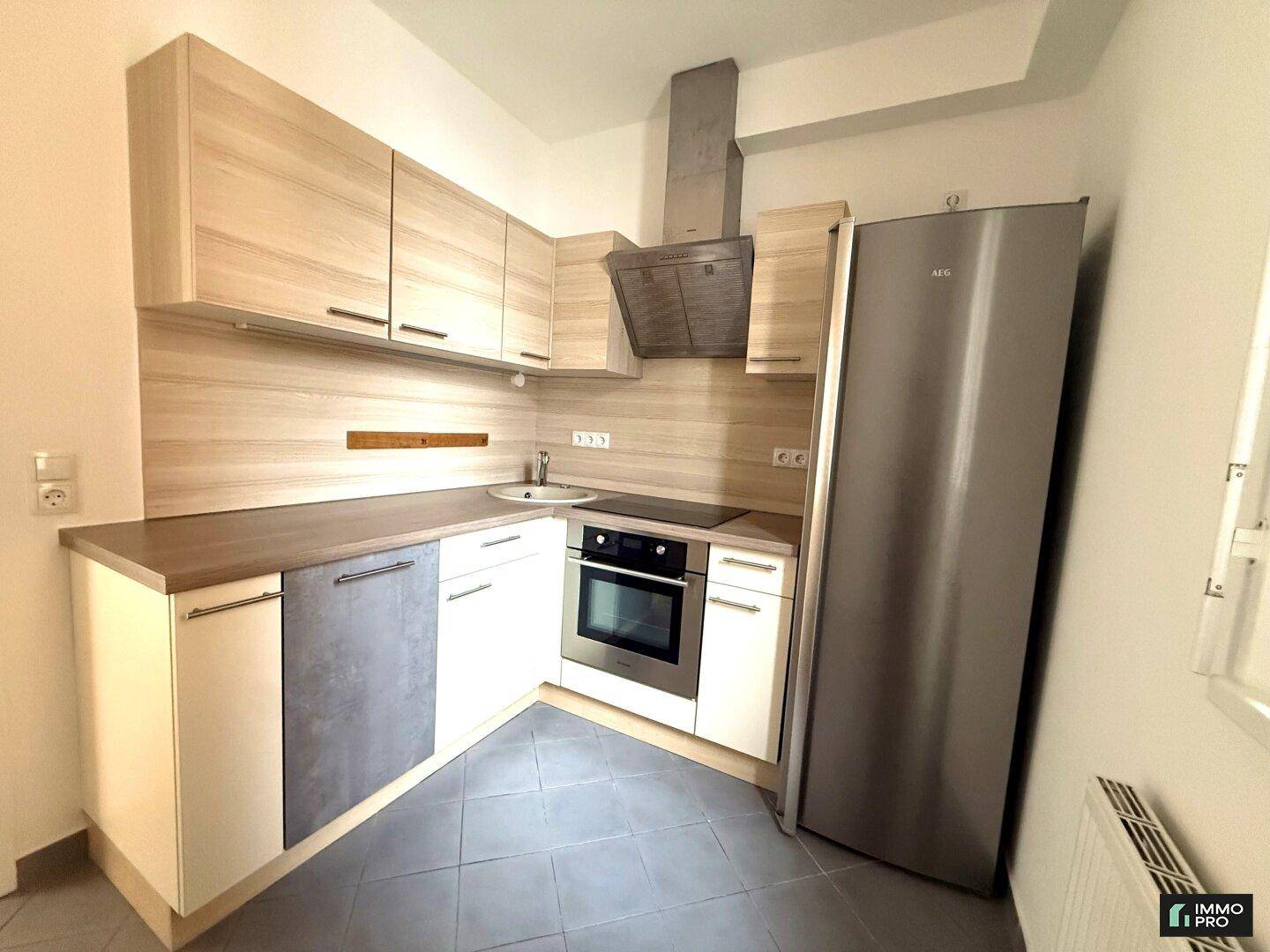 Moderne Einbauküche mit hellen Holzfronten, integrierten Geräten und dunklem Fliesenboden.