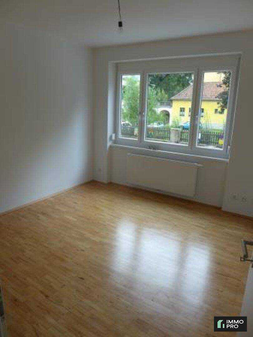 Heller Raum mit Holzparkett und großem Fenster, bietet viel Tageslicht und Ausblick.