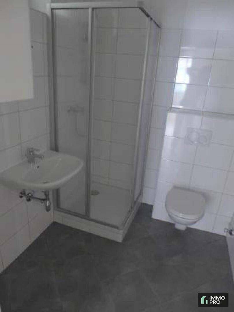 Funktionales Badezimmer mit Duschkabine, Waschbecken und wandhängendem WC, hell gefliest.
