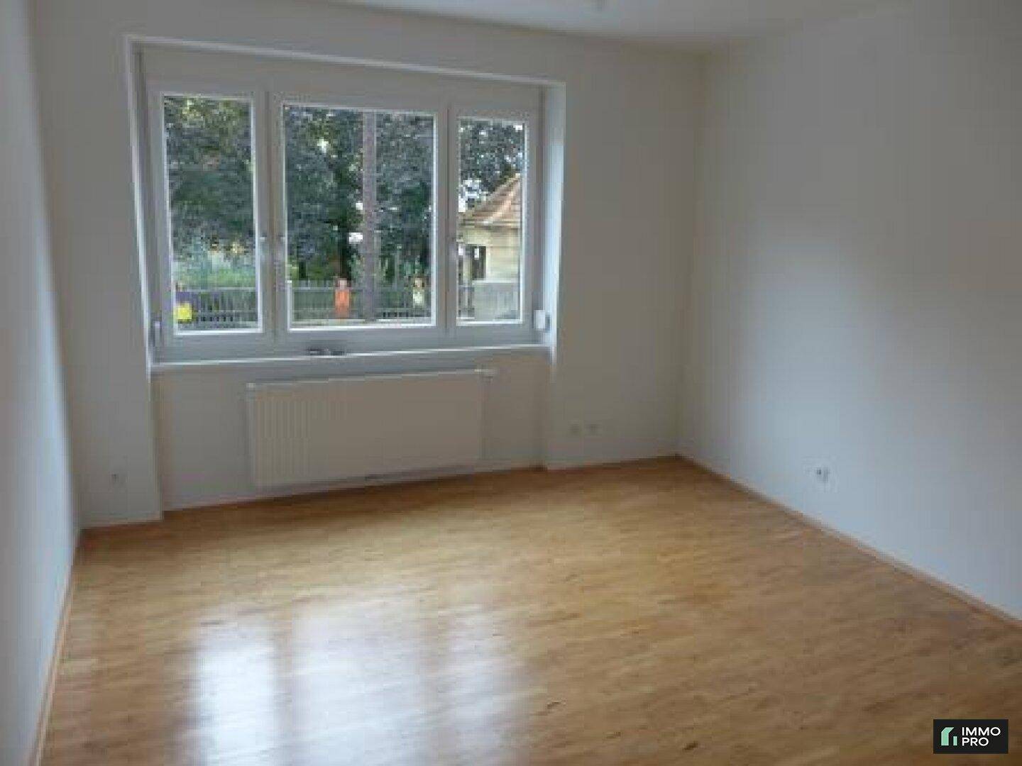 Ruhiges Zimmer mit Parkettboden und großem Fenster, bietet eine angenehme Wohnatmosphäre.