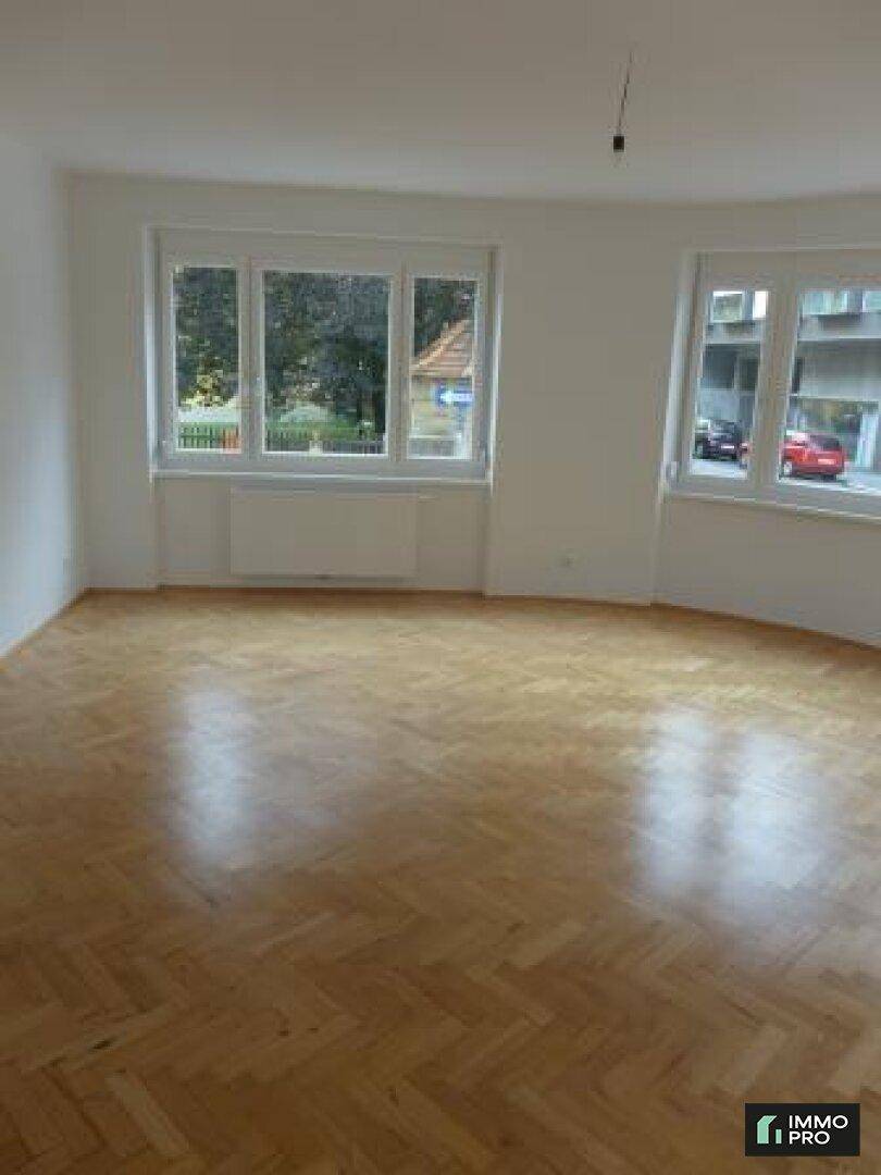 Geräumiges, helles Zimmer mit glänzendem Fischgrätparkett und Blick ins Grüne.