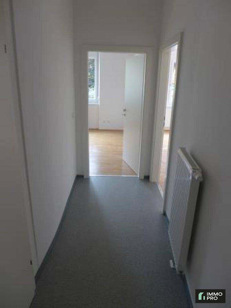 Heller Flur mit grauem Boden und Heizkörper, verbindet verschiedene Wohnbereiche.