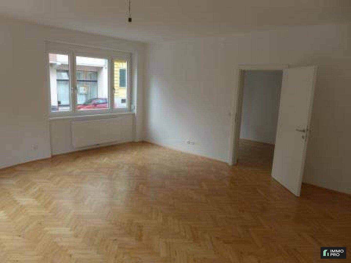 Geräumiges Zimmer mit Fischgrätparkett und Zugang zu weiteren Räumen, hell und einladend.
