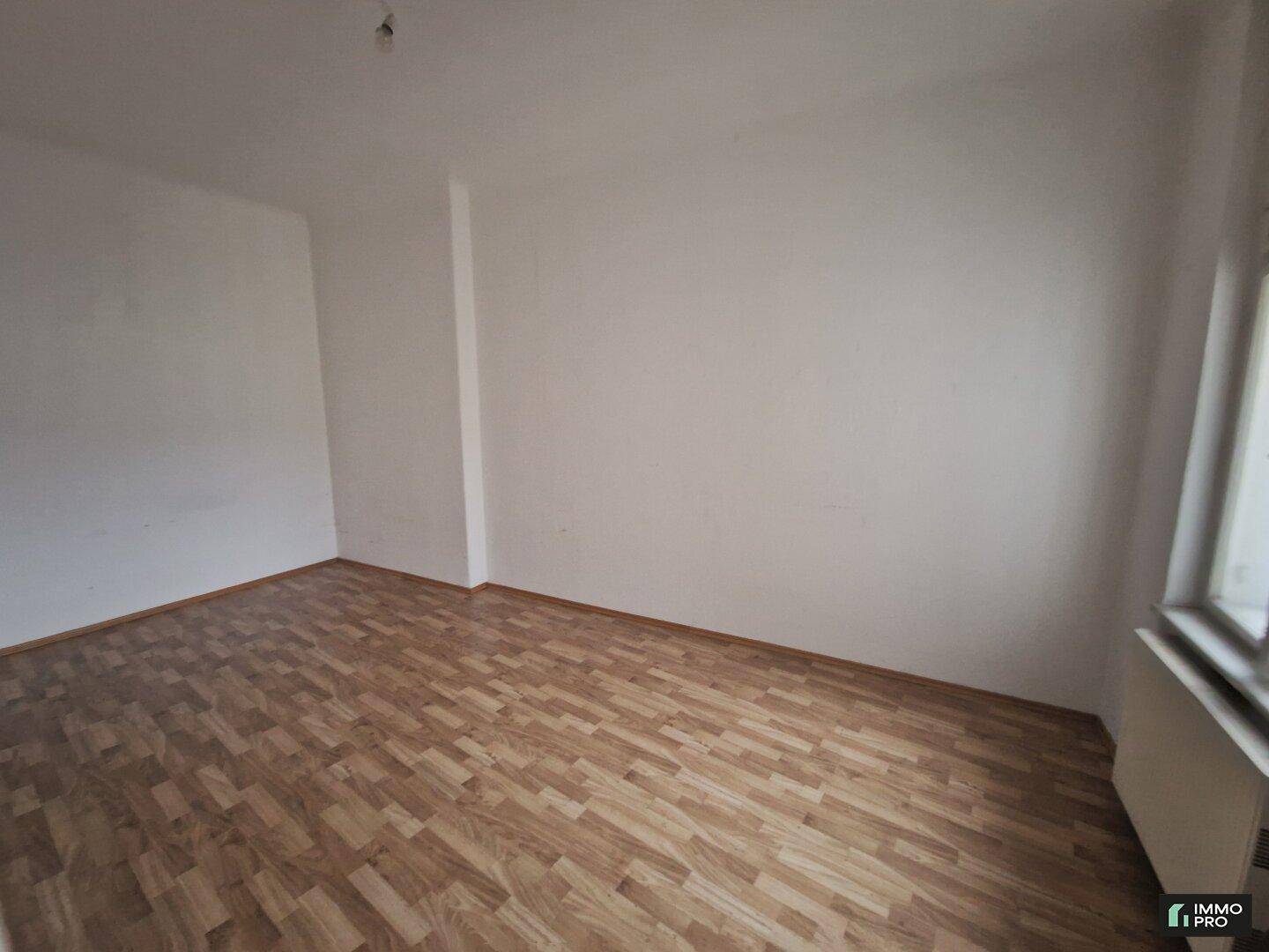 Heller, leerer Raum mit Laminatboden und einem Fenster, bereit zur individuellen Gestaltung.