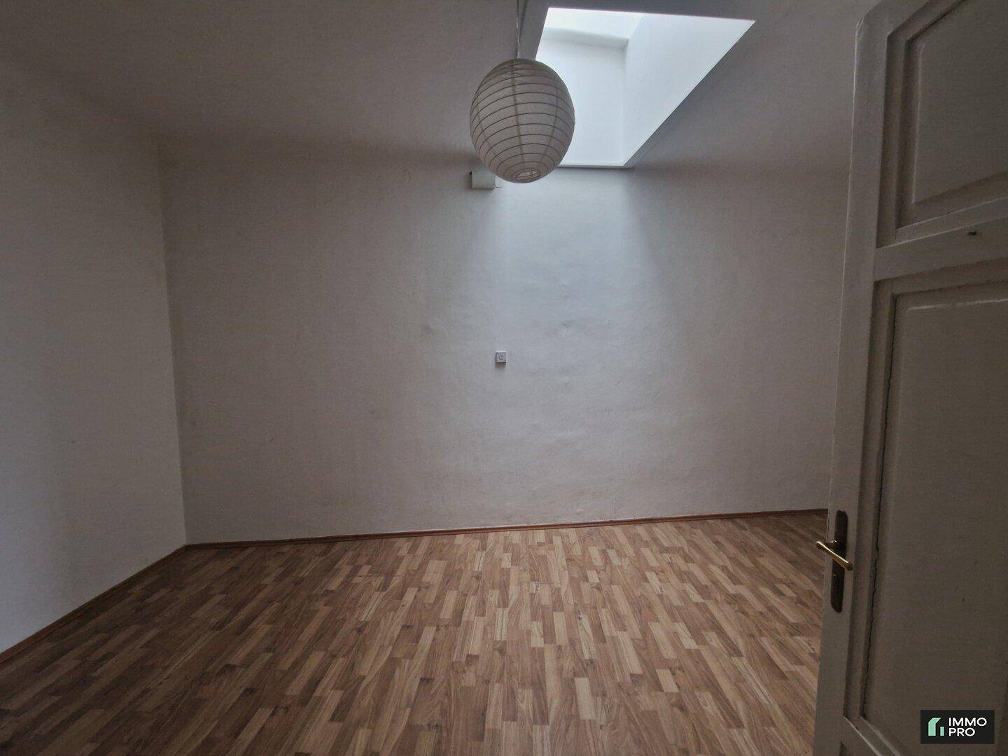 Geräumiger Raum mit Laminatboden, Oberlicht und einer Hängelampe, bietet viel Tageslicht.
