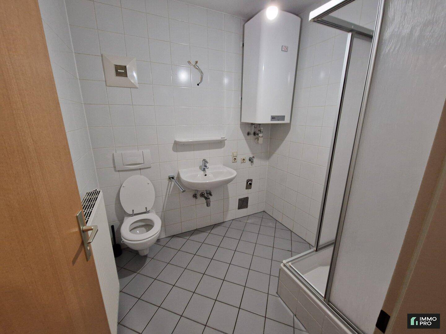 Gefliestes Badezimmer mit Dusche, WC, Waschbecken und Warmwasserboiler im Dachgeschoss.