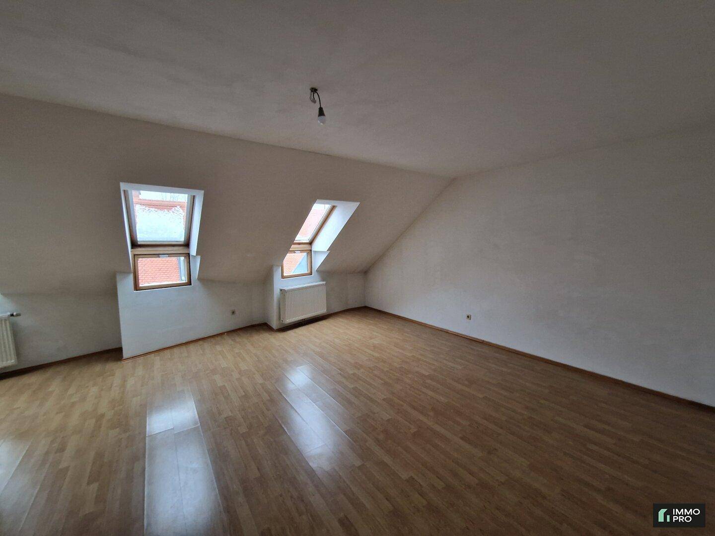 Geräumiger Wohnbereich im Dachgeschoss mit Laminatboden und zwei Dachfenstern für natürliches Licht.