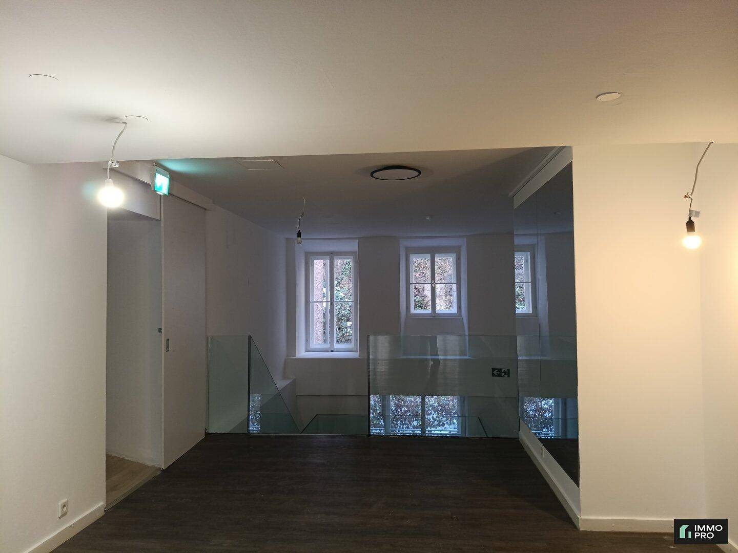 Heller Treppenabsatz mit Glasgeländer und Fenstern, die viel Tageslicht in den Raum lassen.