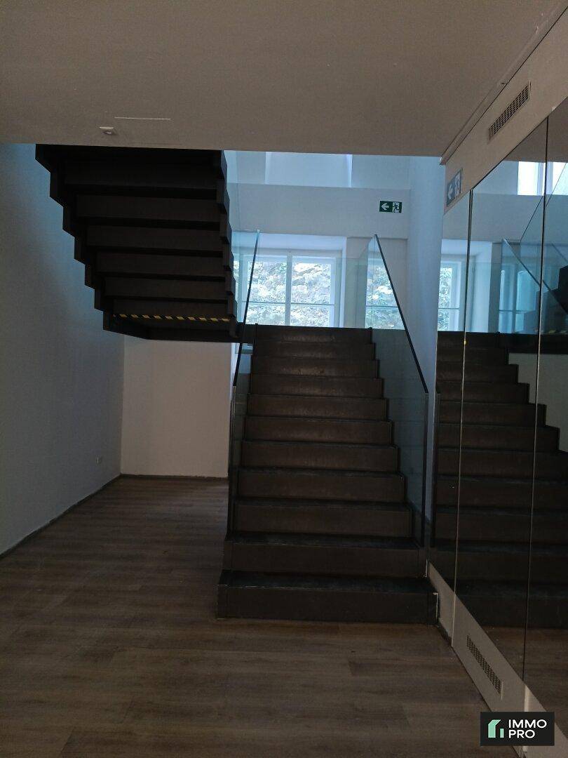 Moderne Treppe mit dunklen Stufen und eleganter Glasbrüstung, die zu den oberen Etagen führt.