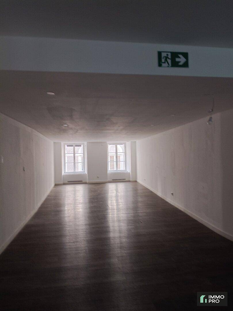Langer, leerer Raum mit dunklem Laminatboden und Fenstern am Ende, ideal für gewerbliche Nutzung.