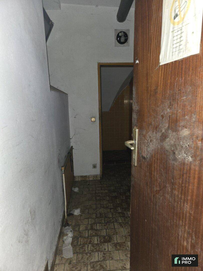 Schmaler Flur mit dunklem Fliesenboden und einer offenen Holztür, die in einen weiteren Bereich führt.