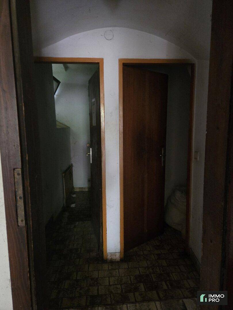 Dunkler Flur mit zwei offenen Holztüren, die zu verschiedenen Räumen führen, und gefliestem Boden.