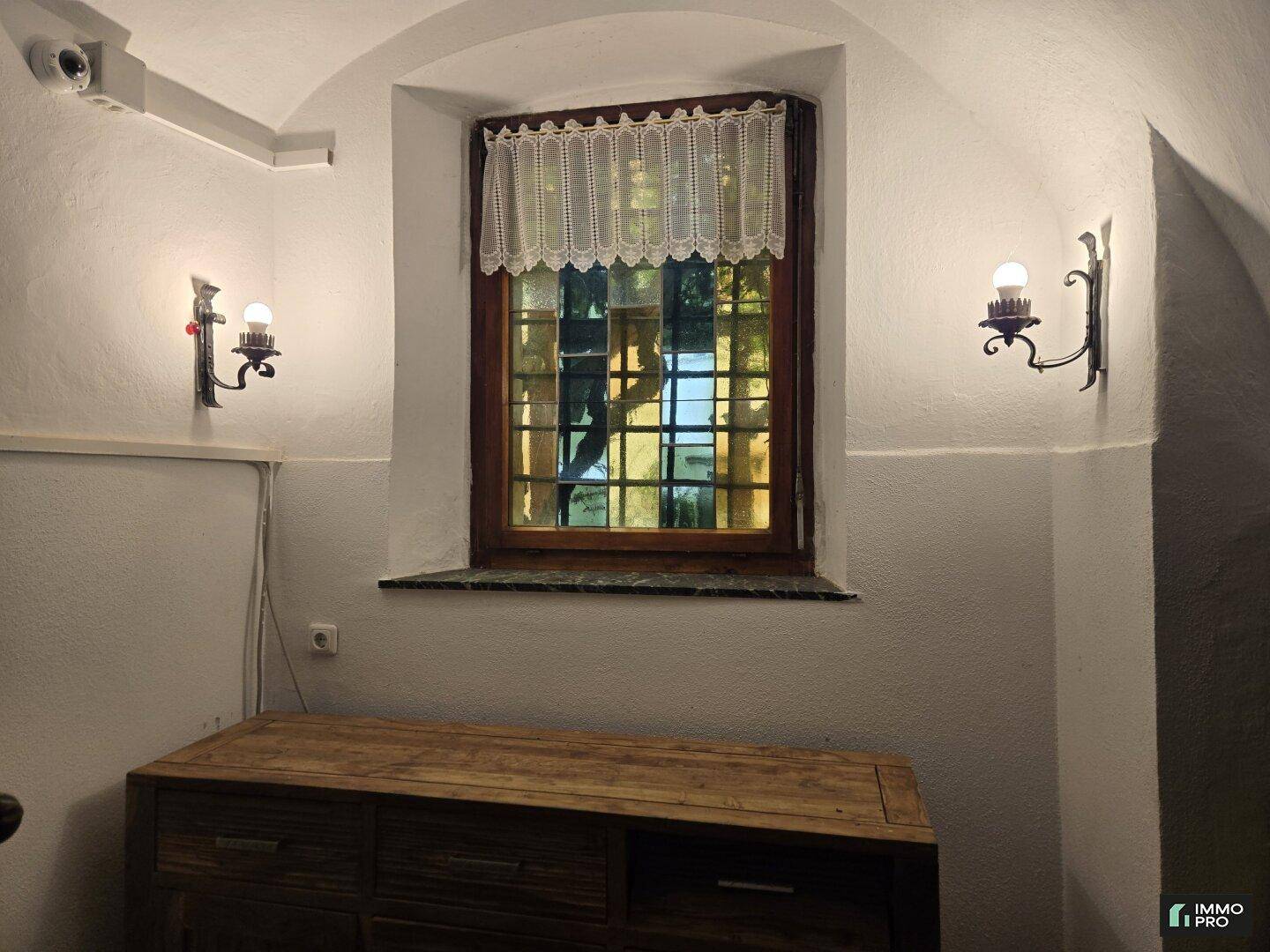 Gemütlicher Flurbereich mit einem Fenster, Wandleuchten und einem Holzschrank unter einem Gewölbe.