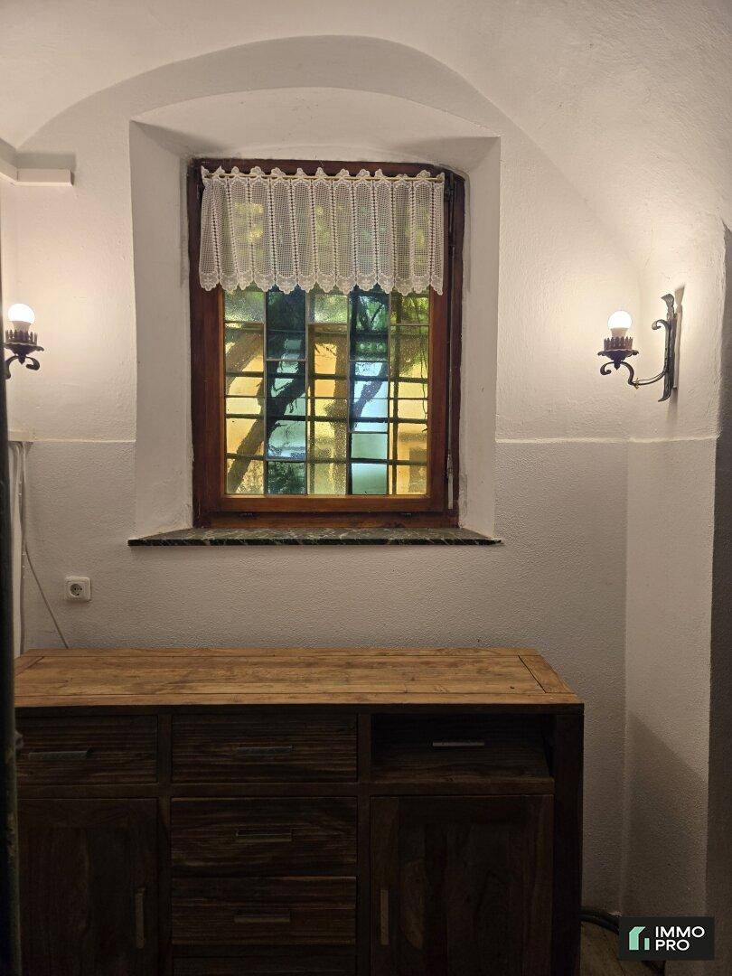 Detailansicht eines Fensters mit Vorhang und Wandleuchten in einem gewölbten Flur mit Holzschrank.