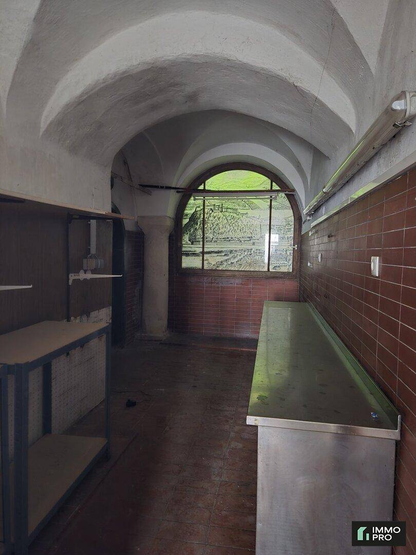 Industrielle Küche mit Gewölbedecke, braunen Wandfliesen und Edelstahlarbeitsflächen, renovierungsbedürftig.