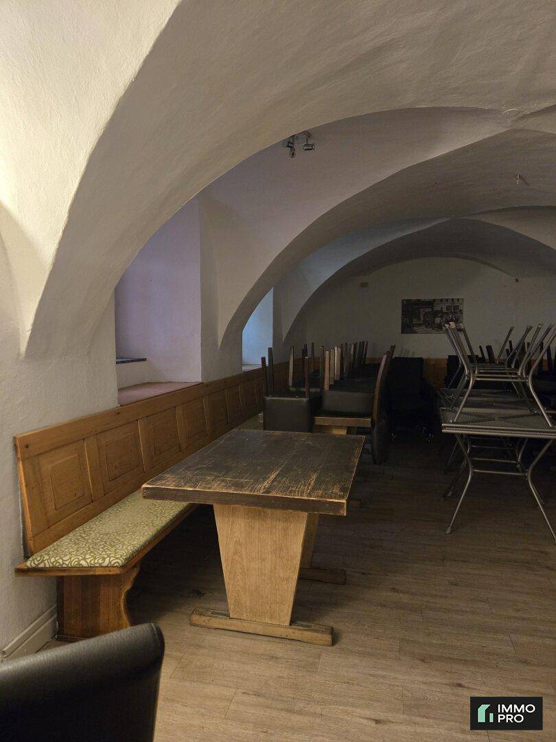 Gastraum mit gewölbter Decke, Holzbänken und Tischen, sowie gestapelten Stühlen, bereit zur Nutzung.