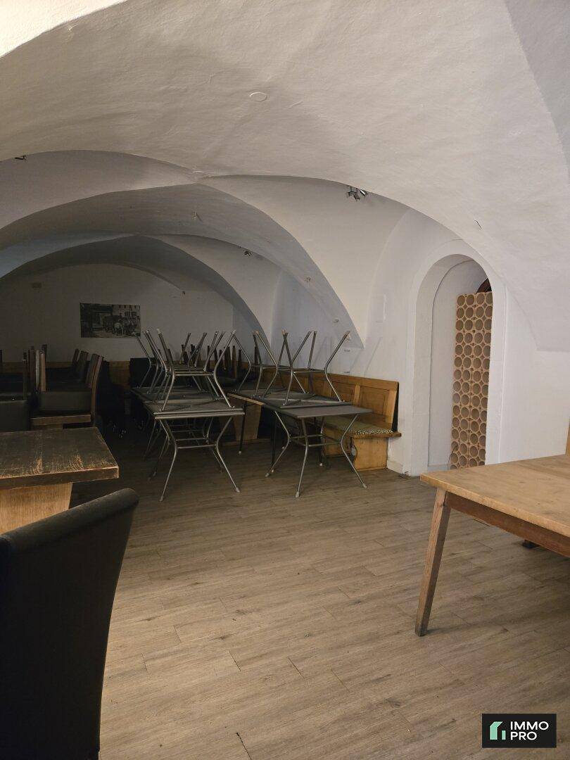 Gastraum mit gewölbter Decke, Holzbänken und Tischen, sowie gestapelten Stühlen, bereit zur Nutzung.