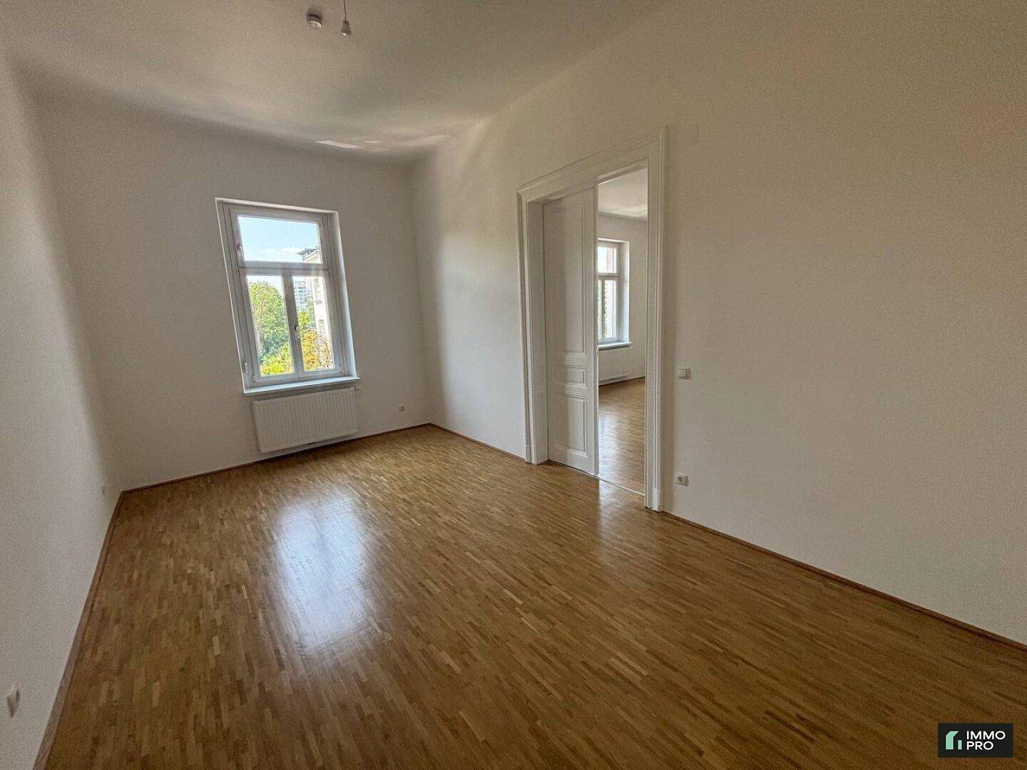 Helles Zimmer mit Parkettboden und Zugang zu einem weiteren Raum, ideal als Schlafzimmer.