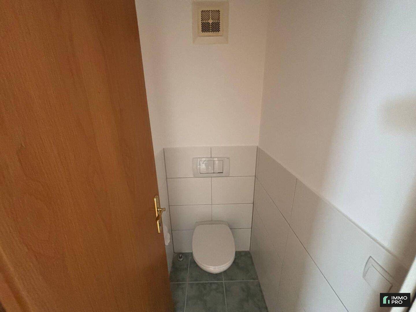 Separate Gästetoilette mit WC, Fliesen und Lüftung an der Decke.