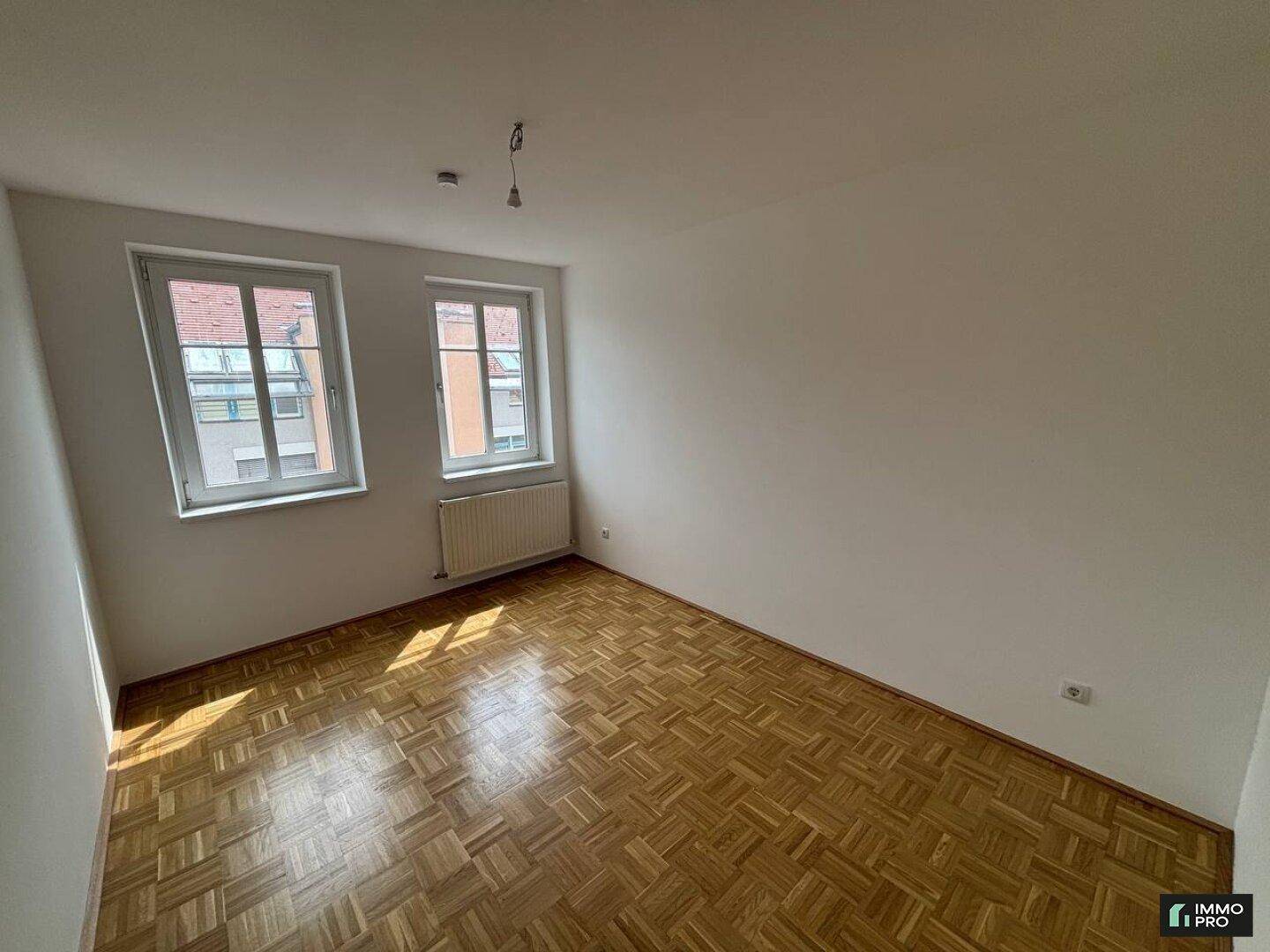 Geräumiges Zimmer mit Parkettboden, zwei Fenstern und viel Tageslicht.