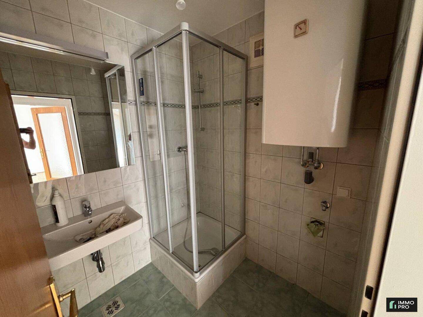 Badezimmer mit Duschkabine, Waschbecken, Spiegel und hellen Fliesen.